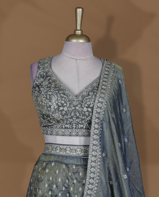 Steel grey and olive ombre effect lehenga set with stitched sleeveless V‑neck embroidered blouse, matching stitched flared lehenga featuring heavy zari and sequin work, and coordinated dupatta with embellished border.