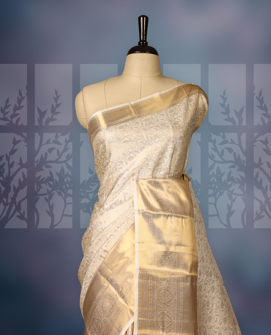 Ivory gold semi silk brocade saree with rich self brocade detailing across the body, paired with an opulent gold woven border and pallu. Comes with a matching blouse for a timeless traditional look.