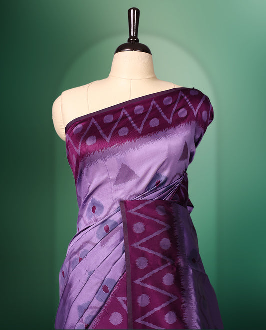 Lavender colour saree featuring subtle woven motifs on the body, enhanced with a deep Purple geometric patterned border, complemented by a rich zari pallu with tassels, and paired with a matching blouse