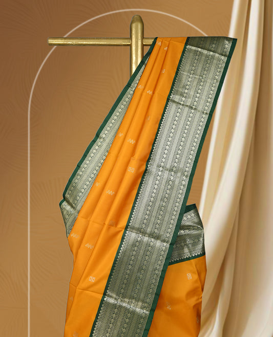 Mustard yellow colour soft silk saree adorned with golden buttas, highlighted by a rich green border and pallu with intricate zari designs & Paired with a matching blouse.
