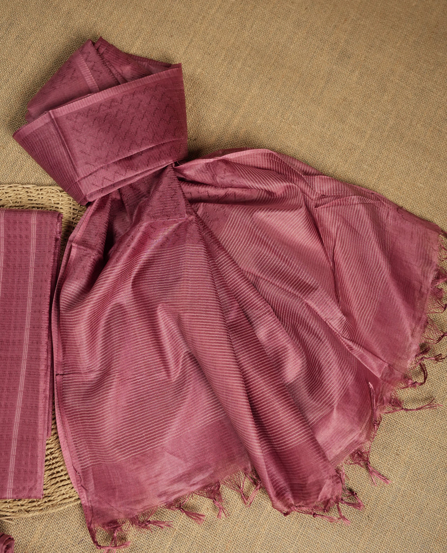 Dusty rose colour tussar suit material featuring a subtle self woven pattern and vertical lines on the body, paired with a lightweight matching dupatta with tassel edges and a plain bottom piece.