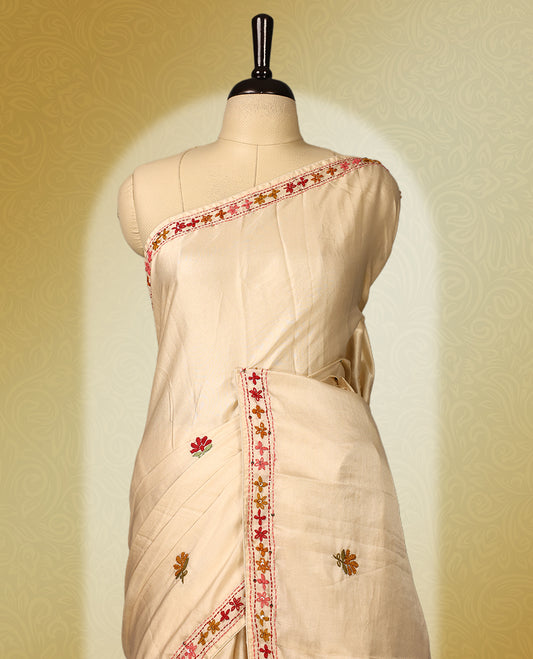 Cream colour pure tussar saree adorned with delicate pink and green floral embroidery along the border and scattered motifs across the body, paired with a matching blouse.