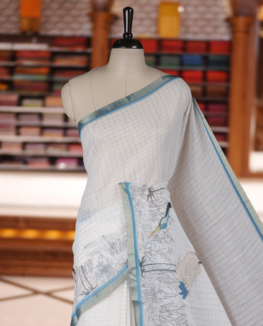 Off white colour Soft cotton saree featuring elegant bird prints along the edges, a stylish checked body, and a beautifully designed blue border & Paired with a matching blouse piece.