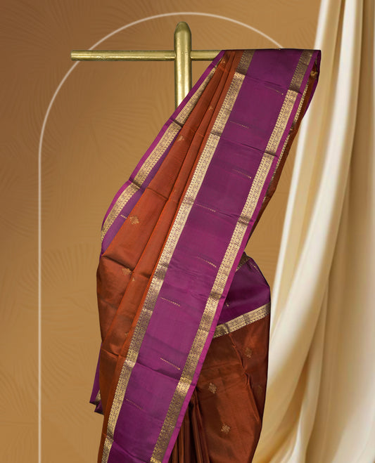 Brown colour soft silk saree adorned with golden zari motifs, complemented by a rich purple border and pallu & Paired with a matching blouse.