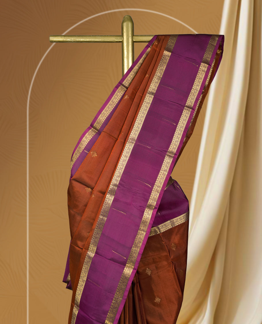 Brown colour soft silk saree adorned with golden zari motifs, complemented by a rich purple border and pallu & Paired with a matching blouse.