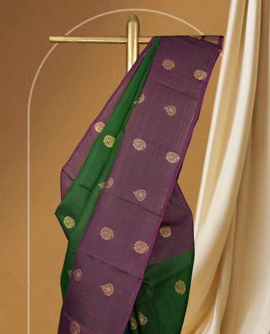 Green colour soft silk saree adorned with golden buttas, complemented by a rich purple border and pallu featuring intricate zari designs & Paired with a matching blouse.
