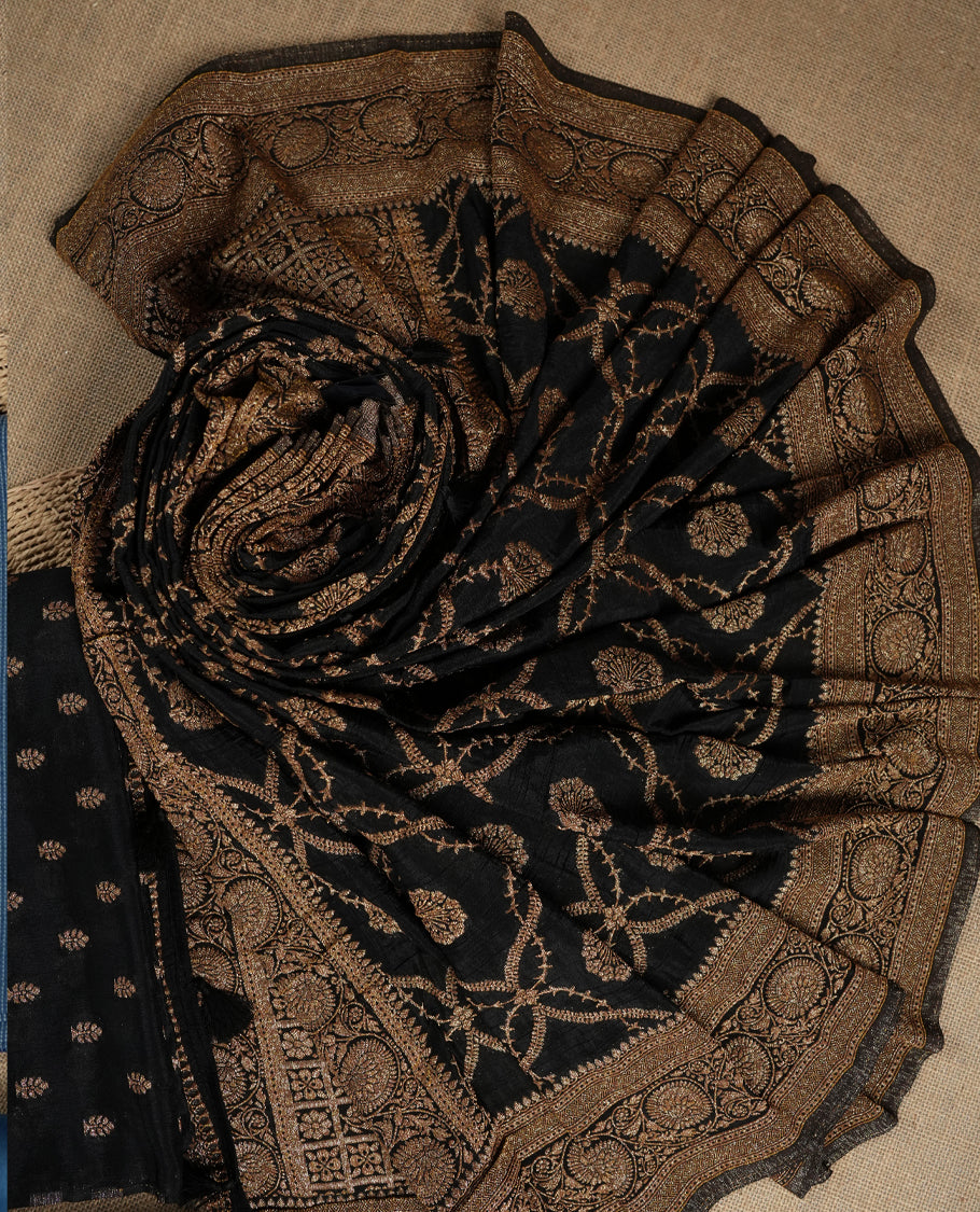 Black suit material adorned with intricate golden zari motifs weaving, exuding timeless elegance & Paired with a beautifully woven dupatta featuring floral and motifs and a matching plain bottom.