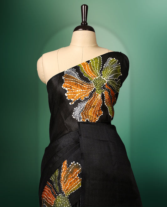 Black colour semi tussar saree adorned with multi colour bold floral motifs across the body, designed without a border for a contemporary touch, and paired with a matching blouse