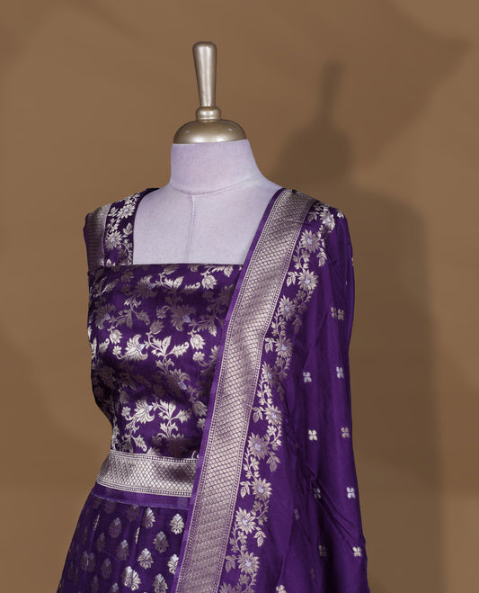 Purple colour Banarasi lehenga set with a stitched flared lehenga featuring all‑over zari butti motifs and rich woven border, paired with an unstitched floral zari blouse piece and matching dupatta with zari border and tasselled edges.