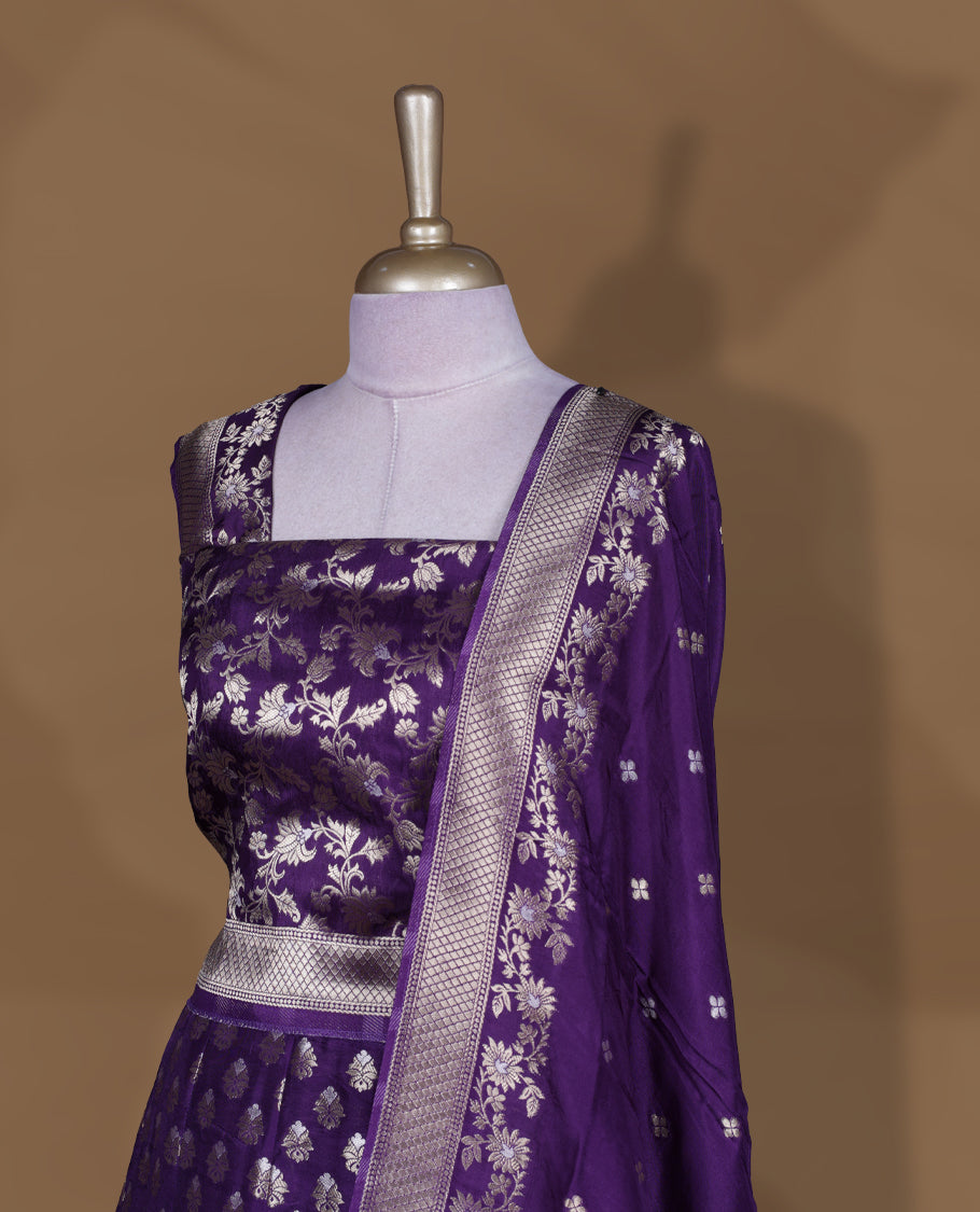 Purple colour Banarasi lehenga set with a stitched flared lehenga featuring all‑over zari butti motifs and rich woven border, paired with an unstitched floral zari blouse piece and matching dupatta with zari border and tasselled edges.