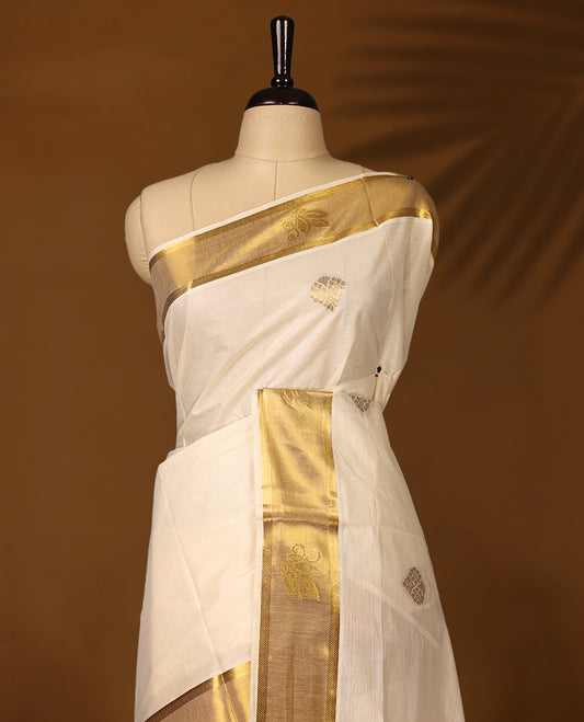 Elegant off white colour cotton Kerala saree embellished with golden buttas across the body and an ornate golden zari border and pallu featuring intricate motifs & A perfect traditional pick, paired with a matching blouse piece.