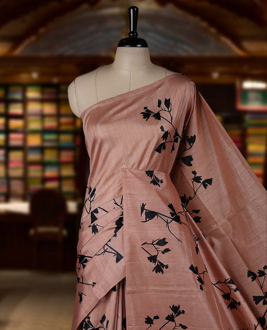 Pastel Peach colour Semi tussar silk saree adorned with black floral prints on the body and an elegant pallu & Comes with a matching blouse piece for a classy look.