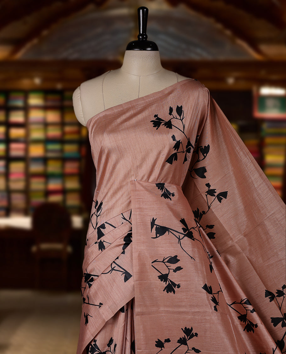 Pastel Peach colour Semi tussar silk saree adorned with black floral prints on the body and an elegant pallu & Comes with a matching blouse piece for a classy look.