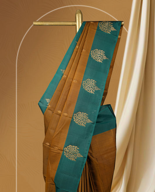 Coffee brown colour soft silk saree adorned with intricate golden zari motifs, teal green colour border for a perfect blend of tradition & Paired with a matching blouse.