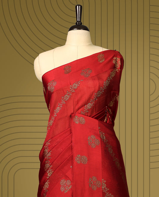 Cherry red semi Banaras tussar saree adorned with golden floral motifs in diagonal patterns across the body and a finely woven zari border, finished with a rich golden pallu, paired with a matching blouse.