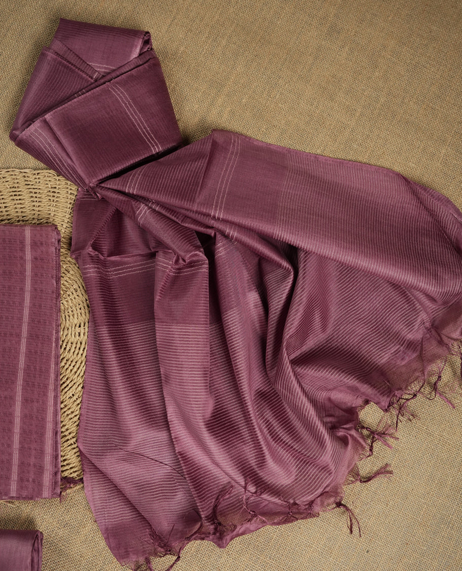 Mauve colour tussar suit material featuring a subtle self woven pattern and vertical lines on the body, paired with a lightweight matching dupatta with tassel edges and a plain bottom piece.