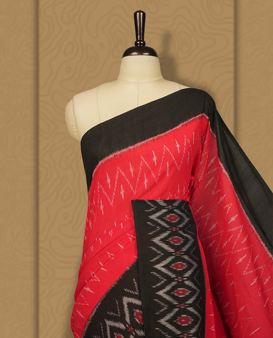 Red colour Ikkat Pochampally saree with bold zigzag motifs and contrasting black borders, The striking woven pallu enhances its elegance, making it a perfect blend of tradition and style.