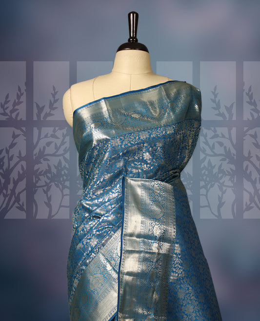 Steel blue semi silk brocade saree featuring intricate silver brocade motifs across the body, enhanced by a gleaming silver woven border and pallu, Paired with a matching blouse for a refined traditional look.