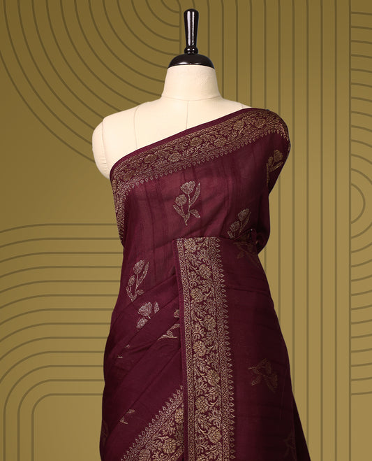 Dark coffee brown colour semi Banaras tussar saree adorned with golden floral motifs along the border and scattered designs across the body, finished with a rich golden zari pallu, paired with a matching blouse.