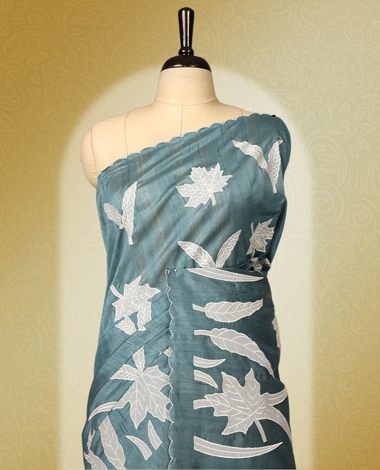 Teal colour semi tussar saree adorned with elegant white applique work in leaf and floral designs across the body and border, paired with a matching blouse.