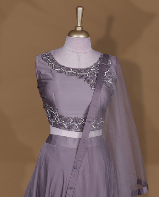 Dusty lavender colour lehenga set with stitched sleeveless blouse featuring intricate bead and sequin embroidery along the neckline and waist, paired with a matching stitched flared lehenga and plain sheer dupatta.