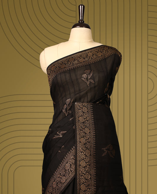 Black semi Banaras tussar saree adorned with golden floral motifs along the border and scattered designs across the body, finished with a rich golden zari pallu, paired with a matching blouse.