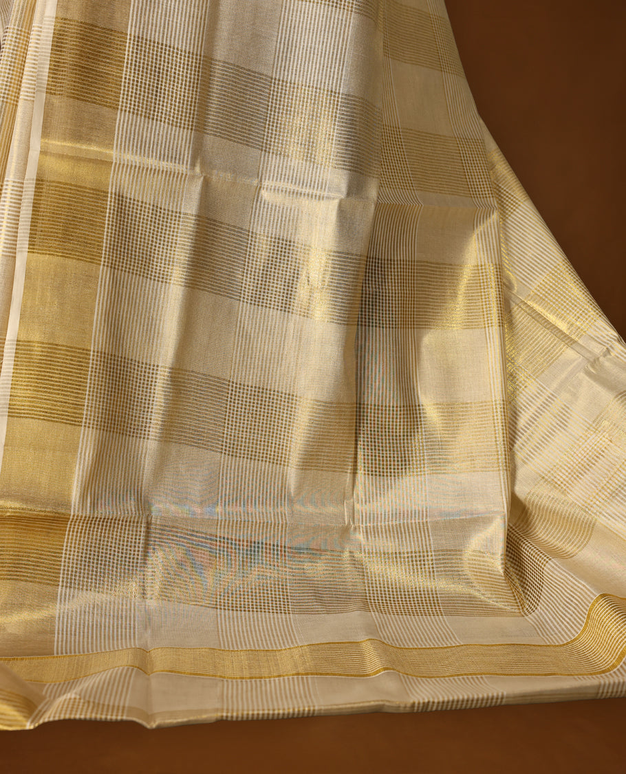 Elegant tissue Kerala saree with a cream base and golden checkered pattern, complemented by a rich golden zari border & Paired with a matching blouse, it's perfect for festive and traditional occasions.