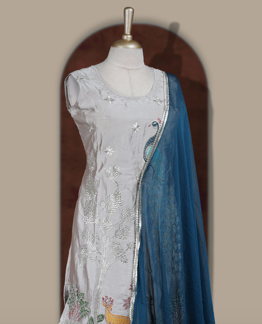 Elegant Ice grey colour embroidered sharara set featuring intricate peacock motifs and delicate stone detailing & Paired with a rich teal blue dupatta edged in silver and flared bottom.