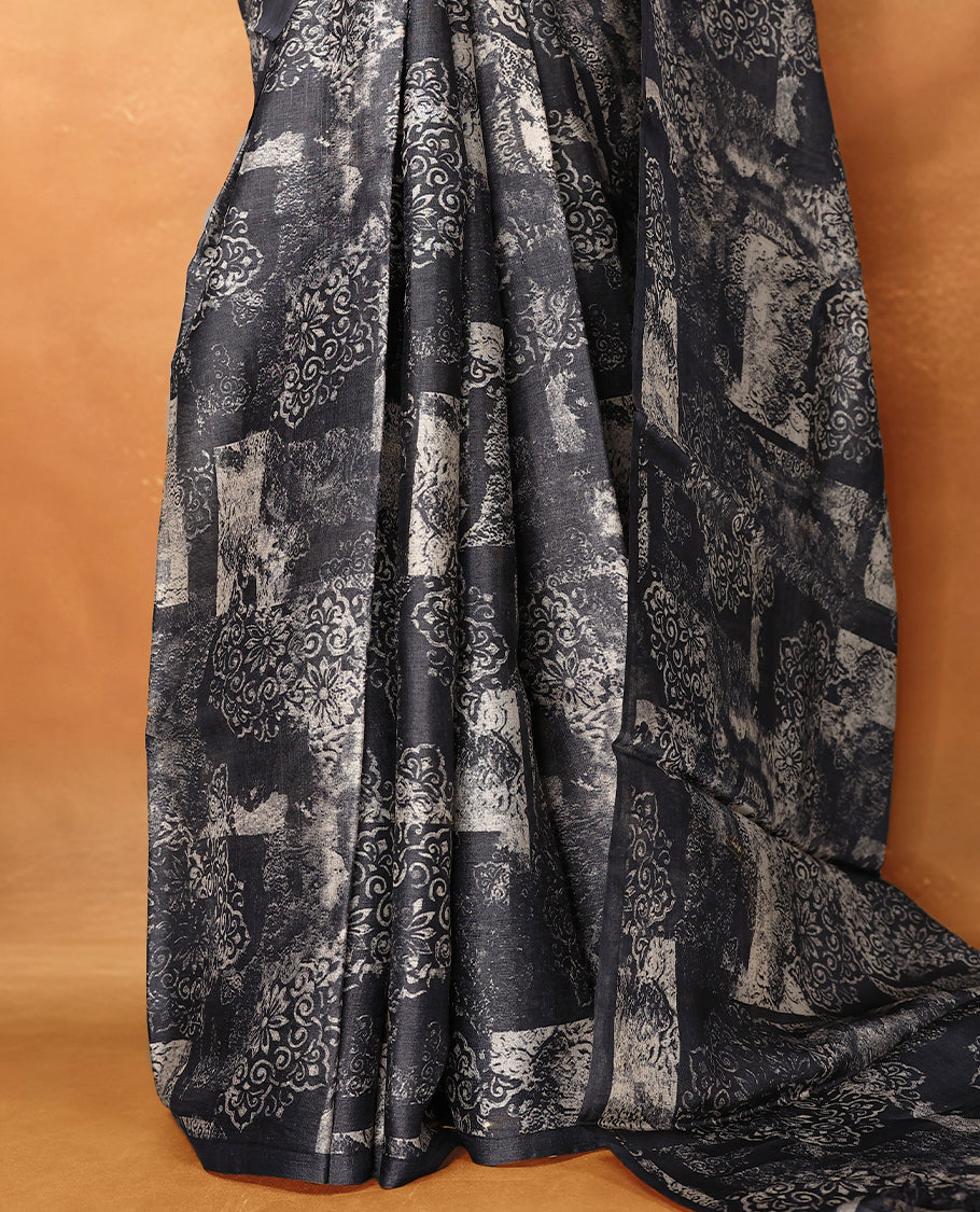 Black colour pure tussar silk light weight saree with full body abstract floral print, no defined border and pallu, paired with matching abstract printed blouse.