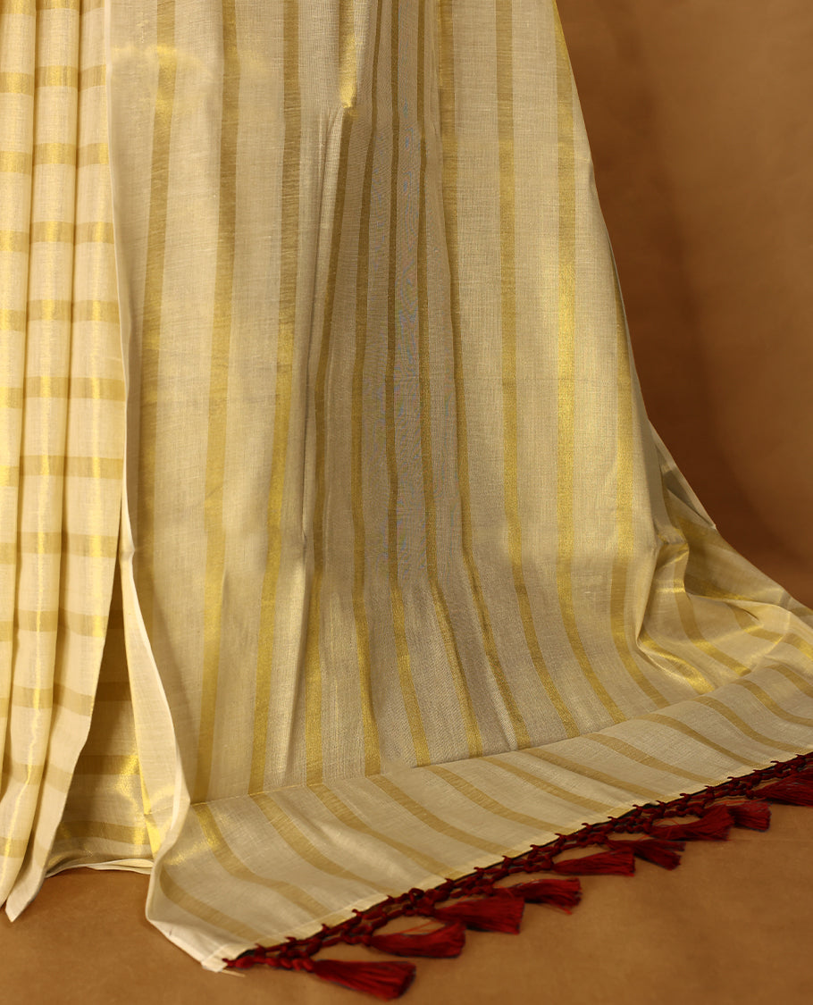 Light Gold colour Tissue Kerala saree featuring Gold zari Striped body, with Maroon colour tassels with a matching blouse perfect for festive occasions.