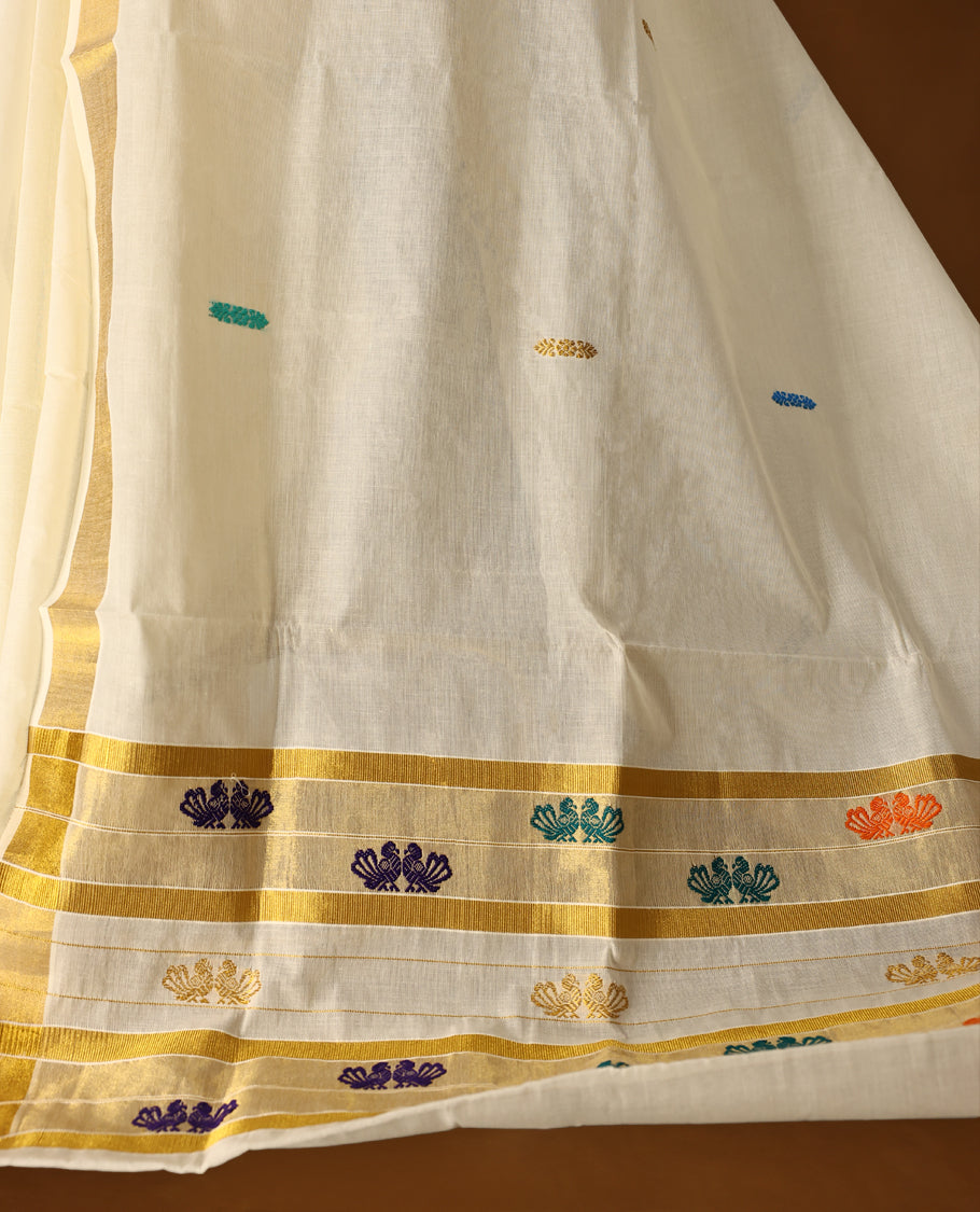 Elegant off white colour cotton Kerala saree featuring a golden zari border, colorful thread buttas, and vibrant peacock motifs on the pallu, and paired with matching blouse.