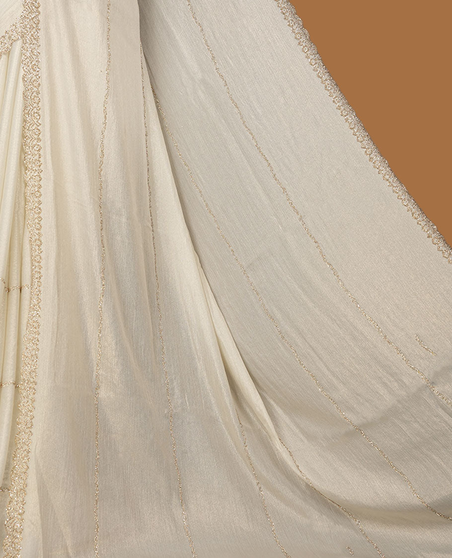 Pastel Cream Colour shimmer fancy saree adorned with scattered gold stone buttas all over the body, paired with a delicate stone worked border and matching blouse