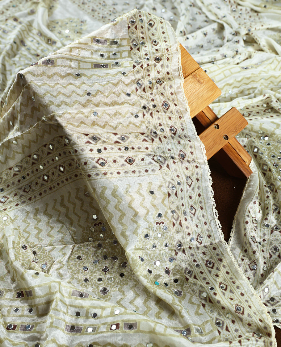 Cream colour churidar material adorned with intricate geometric designs and sparkling mirror work, paired with a plain matching bottom and dupatta.