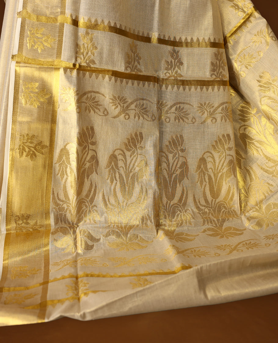 Elegant off white colour tissue Kerala saree featuring rich golden floral motifs and a shimmering zari border, exuding traditional charm and grace, Comes with a matching blouse to complete the timeless look.