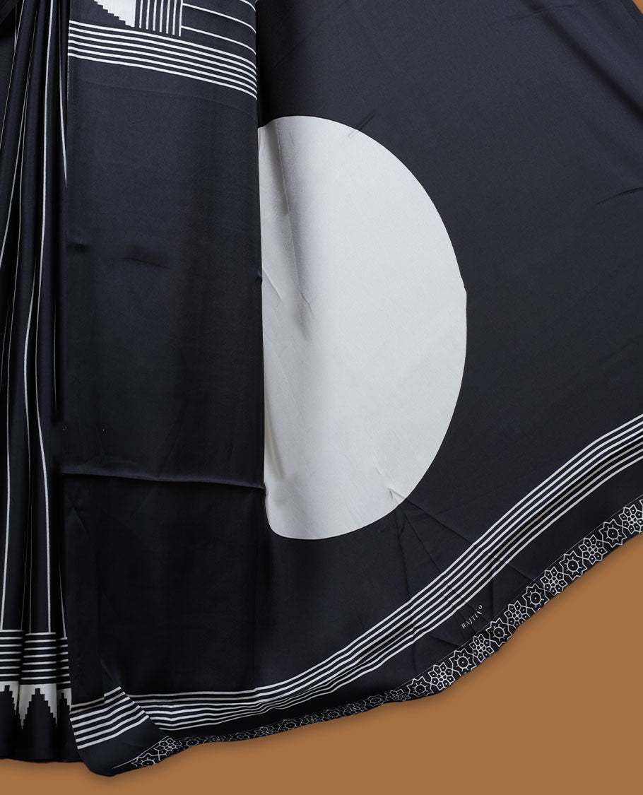 Black colour semi modal saree featuring white colour geometric borders and fine stripe detailing, finished with an oversized circular motif on the pallu, paired with a matching printed blouse.