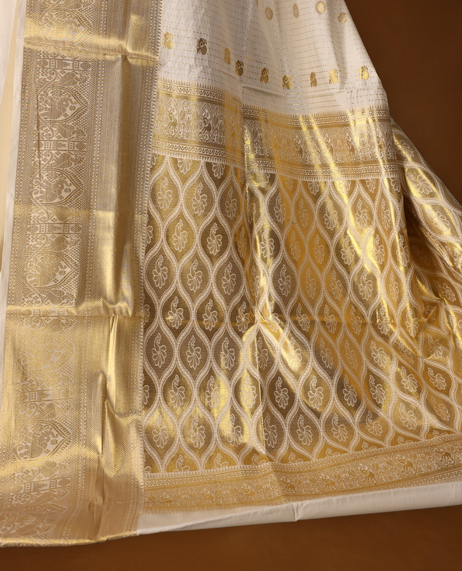 Elegant off white colour cotton Kerala saree with golden buttas, rich zari border, and intricately woven pallu featuring floral and temple motifs. Perfect for festive occasions, paired with a matching blouse.