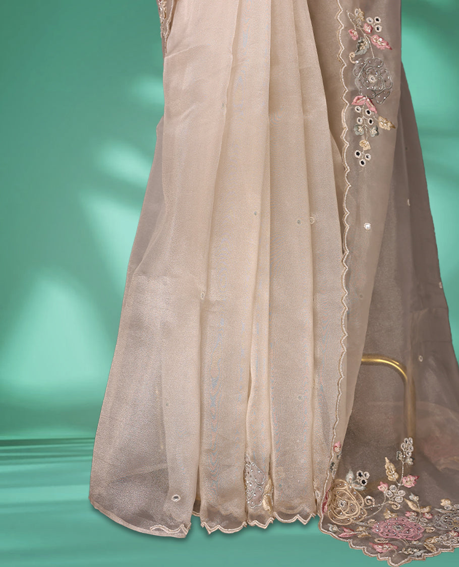 Beige Colour organza saree featuring delicate floral embroidery with applique, bead, mirror, and thread detailing on the body and scalloped border, lending a soft feminine charm, paired with a matching blouse.