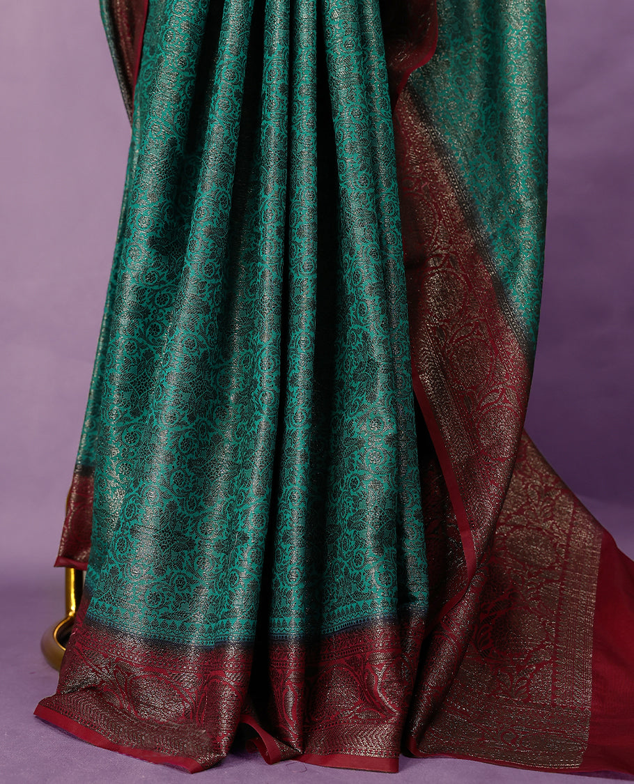 Dark aqua green colour semi Banaras Katan saree featuring an antique zari jacquard body, complemented by a contrasting traditional border with a floral kodi design, paired with a matching blouse.