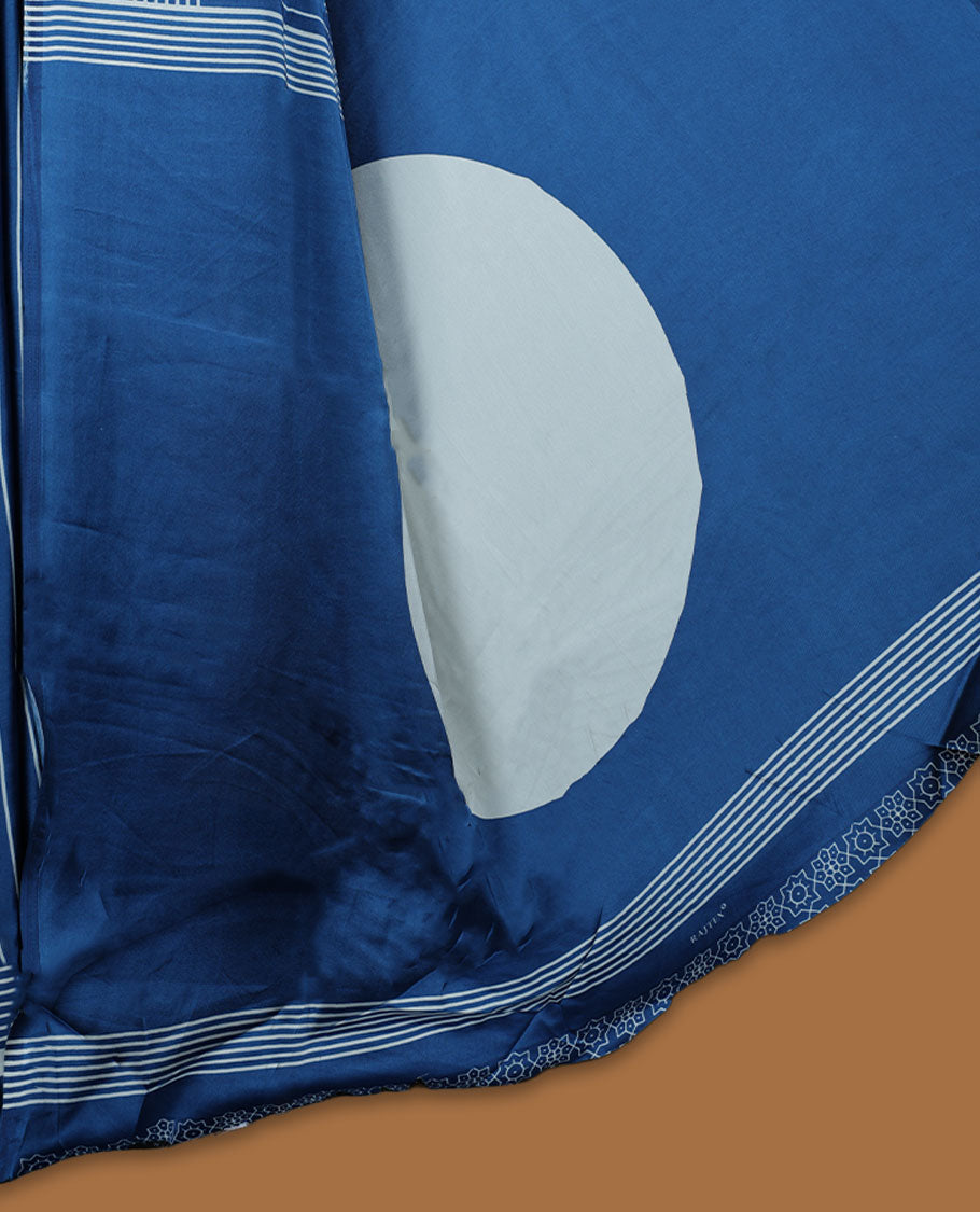 Blue colour semi modal saree highlighted with white triangle border accents and sleek striped detailing across the drape, featuring a bold oversized white circular motif on the pallu, paired with a matching printed blouse.