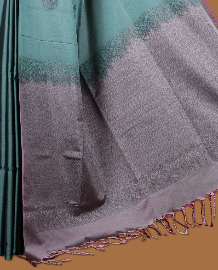 Pine green colour semi soft silk saree adorned with delicate woven floral motifs on the body, complemented by a contrast dusty pink colour woven pallu with intricate detailing and tassel accents without border & Comes with a matching blouse piece.
