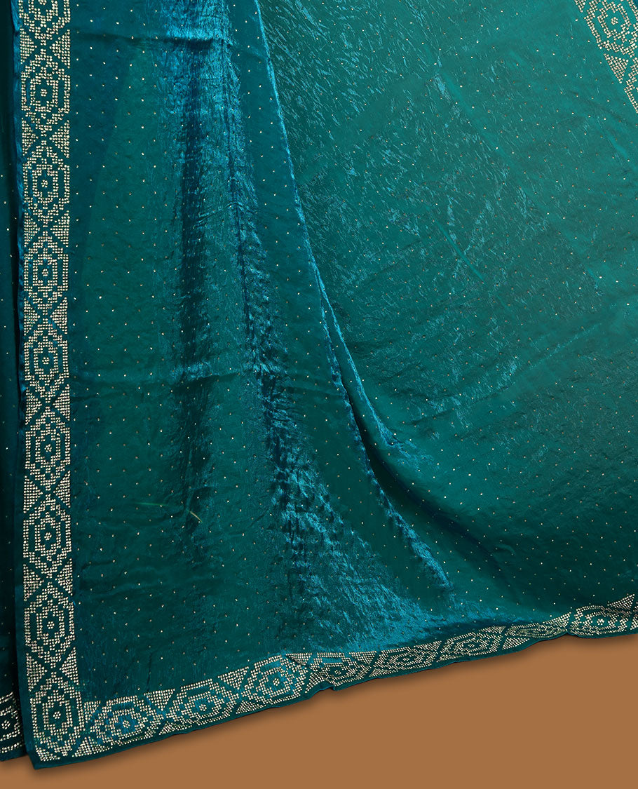 Teal colour chiffon designer saree, featuring delicate scattered stone detailing all over the body, highlighted with intricate stone work and a heavy geometric stone pattern along the border and pallu, paired with a matching embellished blouse.