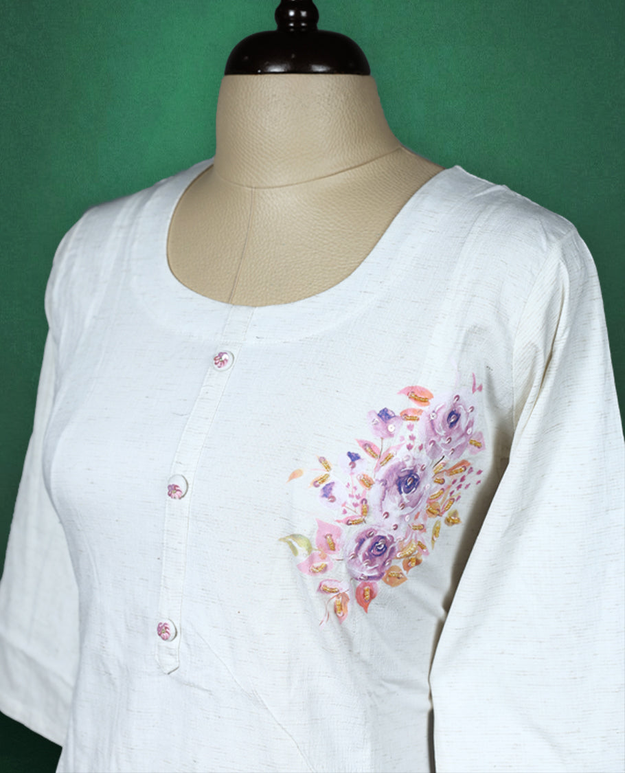 White colour cotton kurti featuring delicate floral prints in soft pastel shades with beads ans sequence work, scoop neckline with button detailing, and elbow length sleeves perfect for a graceful and breezy everyday look.
