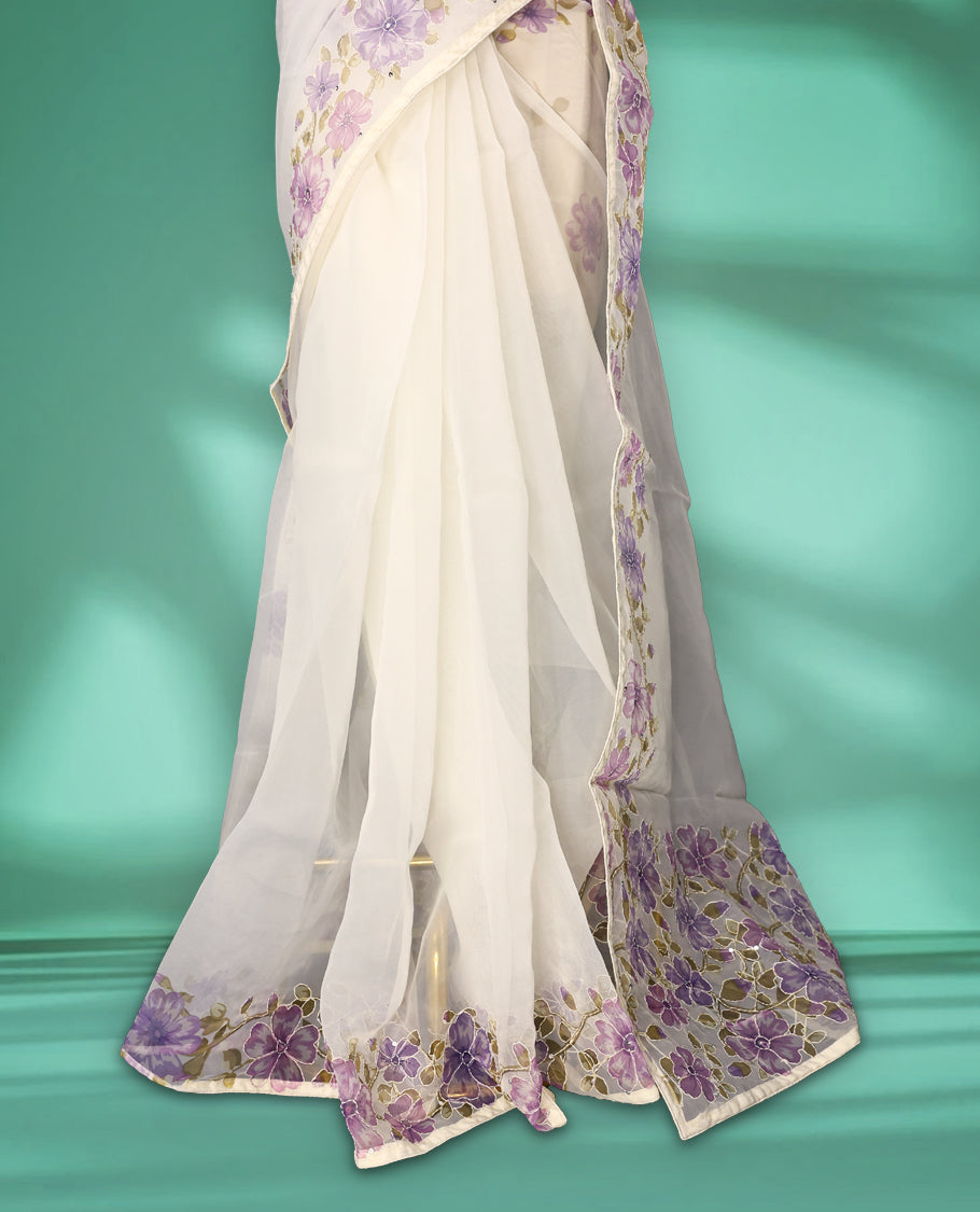 Ivory white colour organza saree adorned with purple floral print with thread detailing on the border and pallu, in a sheer finish that adds elegance, paired with a matching blouse for a graceful look.