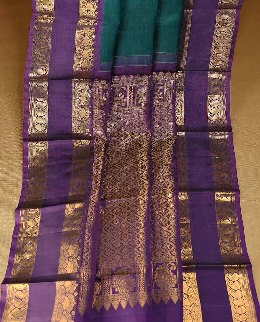Deep teal blue Colour pure Kancheepuram silk saree with small peacock and elephant motifs, featuring a deep purple border with arched floral and paisley gold zari patterns, paired with a matching blouse.