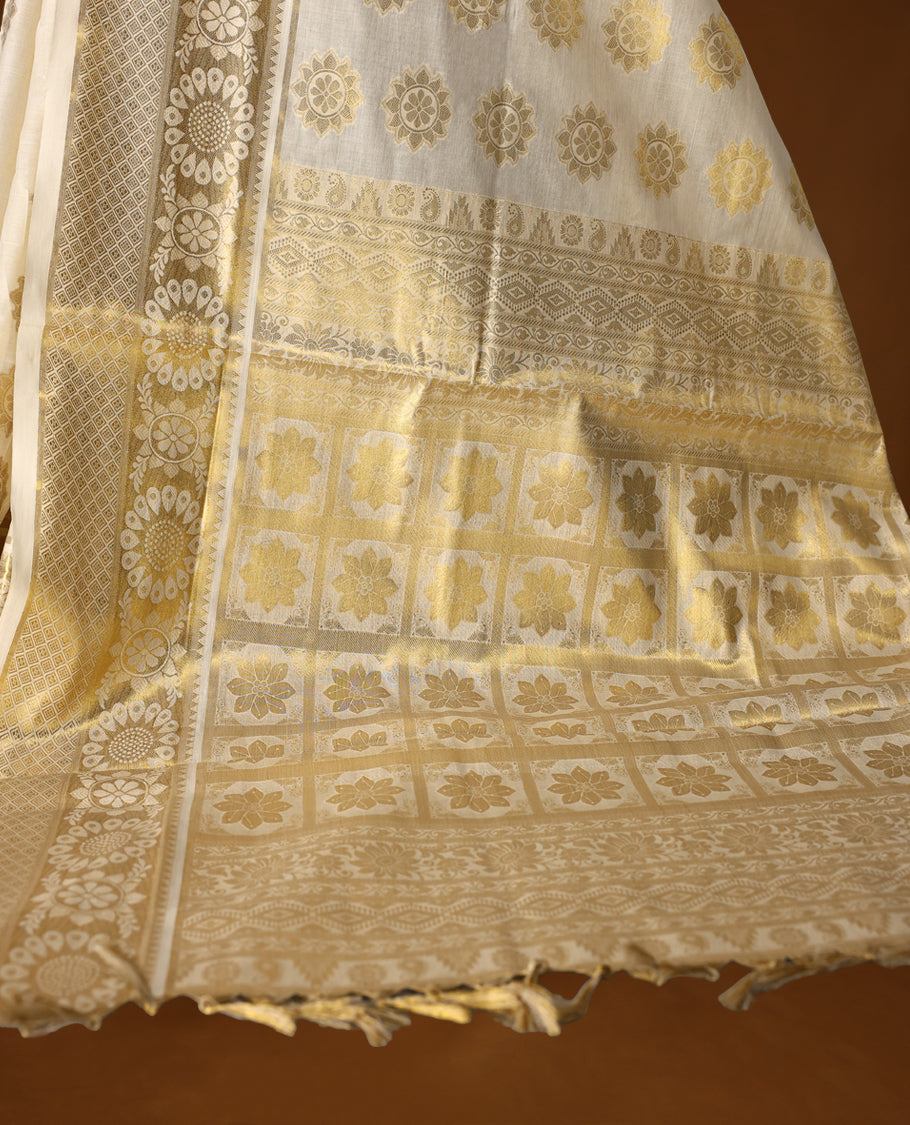 Elegant off white colour soft cotton Kerala saree adorned with golden floral motifs all over, accentuated by an ornate golden pallu with tassels, and a matching blouse, making it a perfect choice for traditional and festive celebrations.