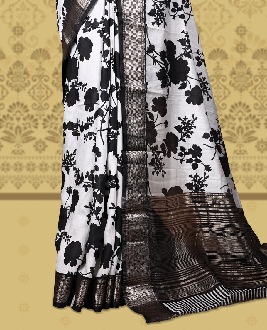 White colour saree adorned with bold black floral prints and a rich black zari border and stripped checkered pallu & Comes with a matching blouse piece.
