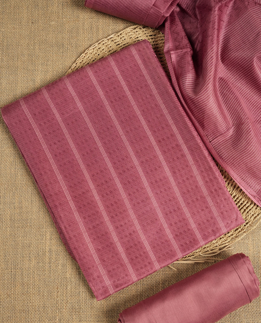 Dusty rose colour tussar suit material featuring a subtle self woven pattern and vertical lines on the body, paired with a lightweight matching dupatta with tassel edges and a plain bottom piece.