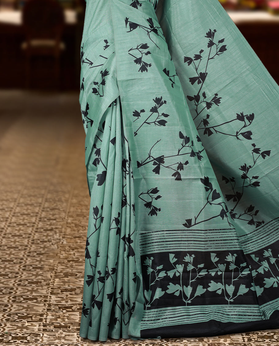 Pastel Green colour Semi tussar silk saree adorned with black floral prints on the body and an elegant pallu & Comes with a matching blouse piece for a classy look.