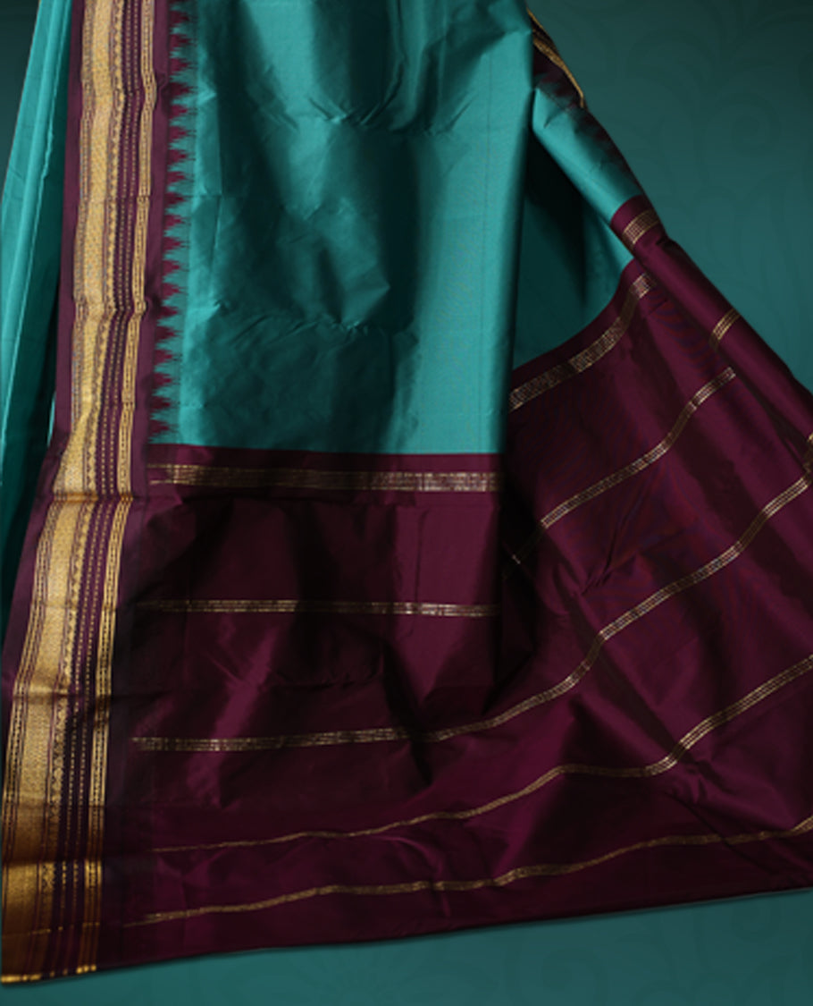 Peacock green semi silk saree with plain body, vibrant deep violet pallu and matching violet border adorned with golden zari, accented with temple motifs along the edges, Paired with a matching blouse, perfect for festive occasions.