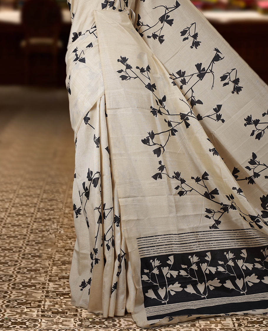 Pastel Ivory colour Semi tussar silk saree adorned with black floral prints on the body and an elegant pallu & Comes with a matching blouse piece for a classy look.